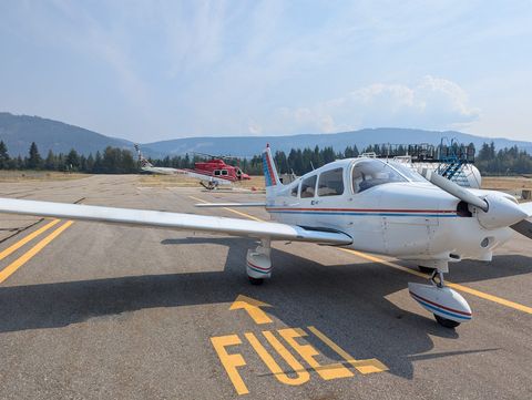 The club's white Piper Warrior II, C-GBNY, parked beside the fuel pad at Salmon Arm airport, with a red helicopter and forested hills behind