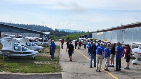 Visitors and airport crew in blue shirts walking the flightline past rows of light aircraft during a fly-in