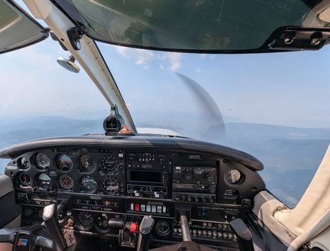 The view from GBNY's cockpit in flight: the instrument panel, and hazy forested hills below through the windscreen