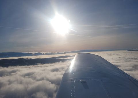 The sun over a sea of cloud filling the valleys, seen past the wing