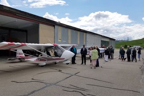 Club members chatting on the ramp beside a white and red light aircraft parked outside the hangars at Salmon Arm airport